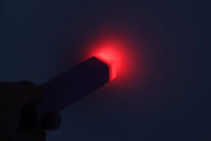 暗闇の中で薄紫色の防犯ブザーの赤いライトが点滅している様子