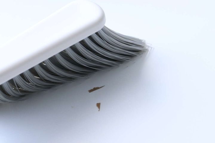 白いテーブルの上で、ブラシの毛先が木くずのようなゴミを掃き集めている様子をクローズアップ。