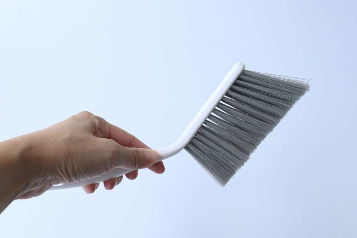 手がベージュ色のブラシを横から持っている様子。ブラシの柄のカーブがわかる。