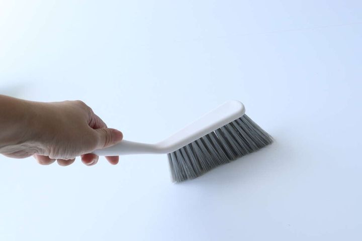 手がベージュ色のブラシを上から持っている様子。ブラシの柄のカーブがわかる。