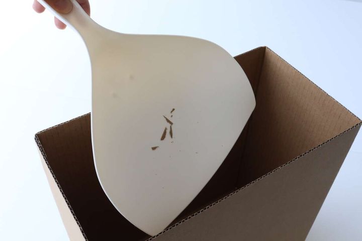 手が、木くずのようなゴミが入ったベージュ色のチリトリを段ボール箱のゴミ箱に捨てようとしている。