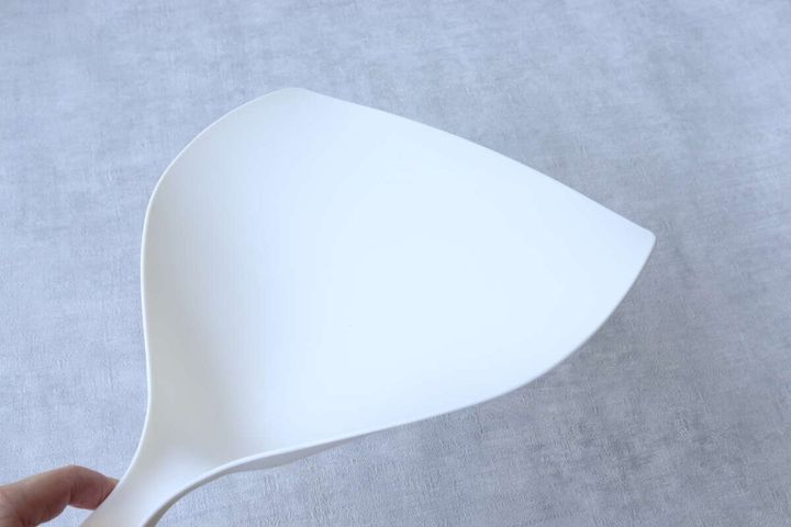 手がベージュ色のミニチリトリの先端部分を持っているクローズアップ。チリトリの薄さがわかる。