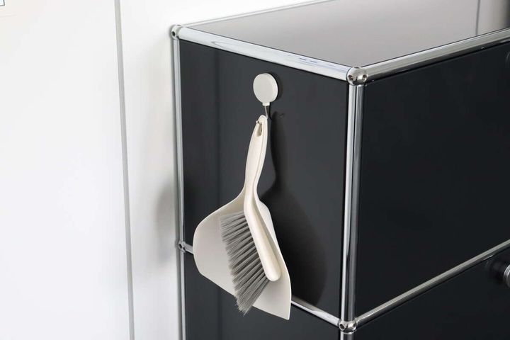 黒い収納棚の側面に、白いフックでベージュ色のミニチリトリとブラシが吊り下げて収納されている。