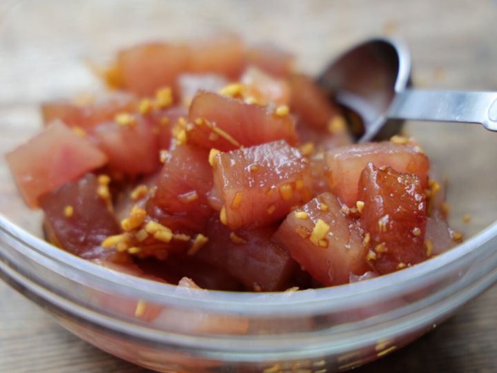 透明なボウルの中で、角切りにされたまぐろと調味料が和えられている様子。