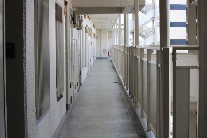 マンションの共用廊下が奥まで一直線に続き、玄関ドアが並んでいる通路の昼間の風景