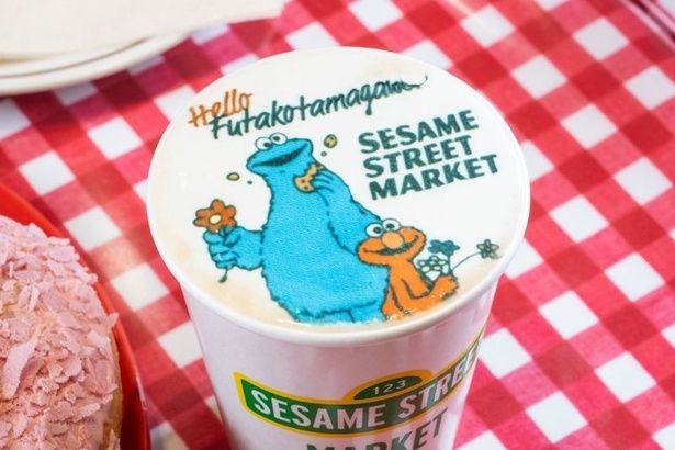 セサミストリートマーケット 玉川高島屋S.C.店限定デザインの「キャラクターラテ」(650円)。“Hello, Futakotamagawa”の文字とともに、花を手に持ったエルモとクッキーモンスターが描かれている