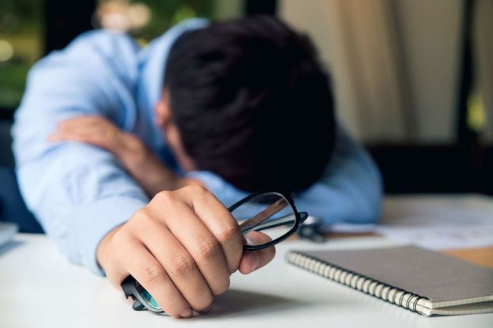 眼鏡を握って机で眠る若者