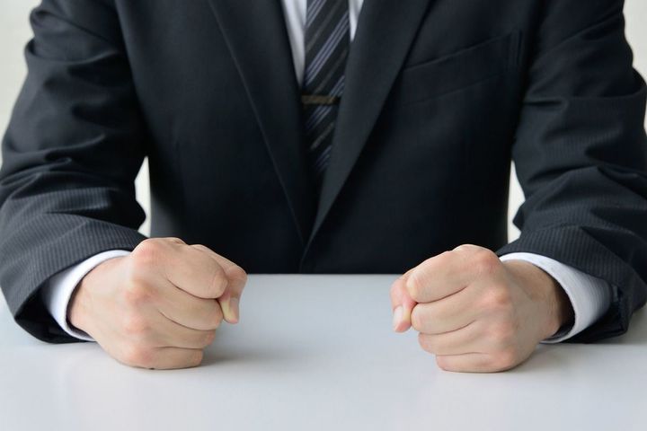 机に握りこぶしを置いたビジネスマン