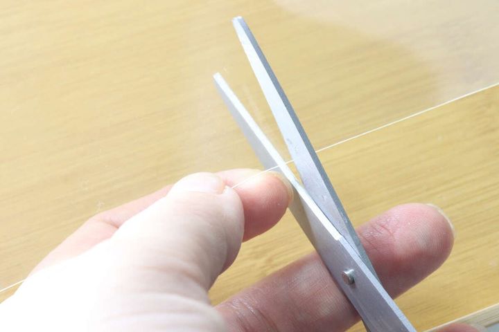 ハサミで透明な粘着ゲルシートをカットしている手元