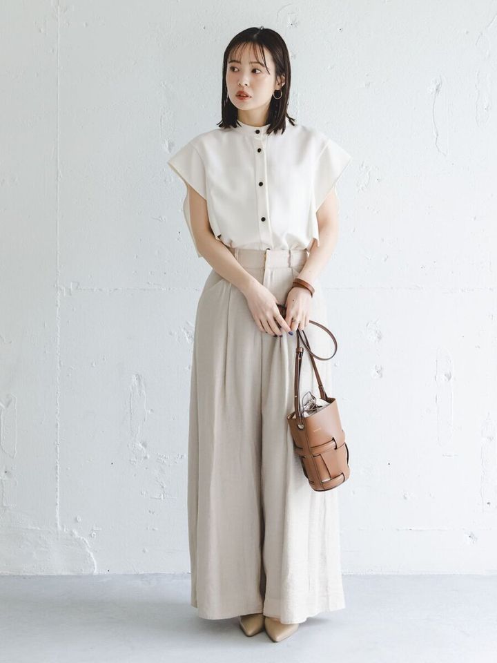 白ブラウスとベージュワイドパンツを着用し、茶色のバッグを持つ女性