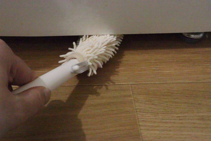 冷蔵庫の下の狭い隙間をハンディモップで掃除する手元
