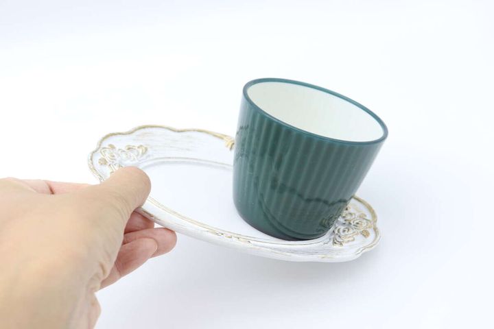 手で傾けた白いミニトレーからコップが滑り落ちる様子