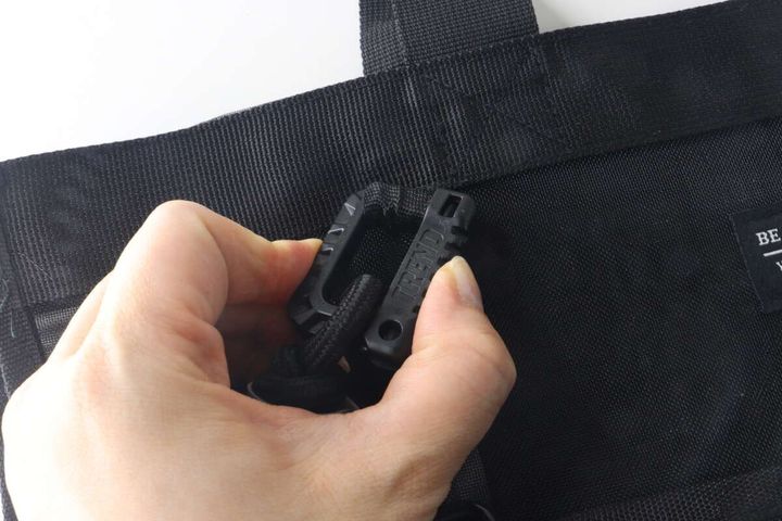 女性の指がバッグに取り付けられたキーホルダーの開閉部分を操作している様子