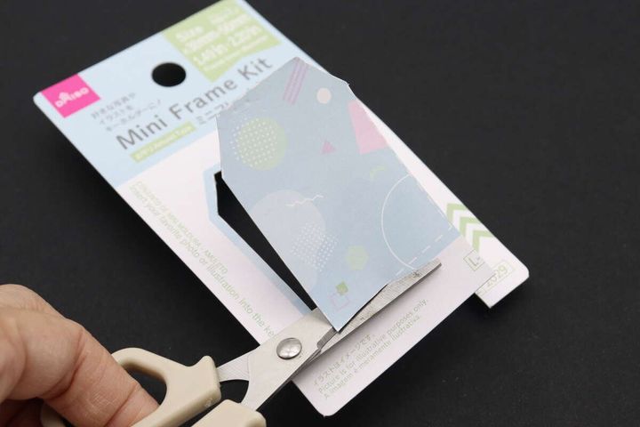 ハサミでミニフレームキットのパッケージ台紙をガイドに沿って切り抜いている手元