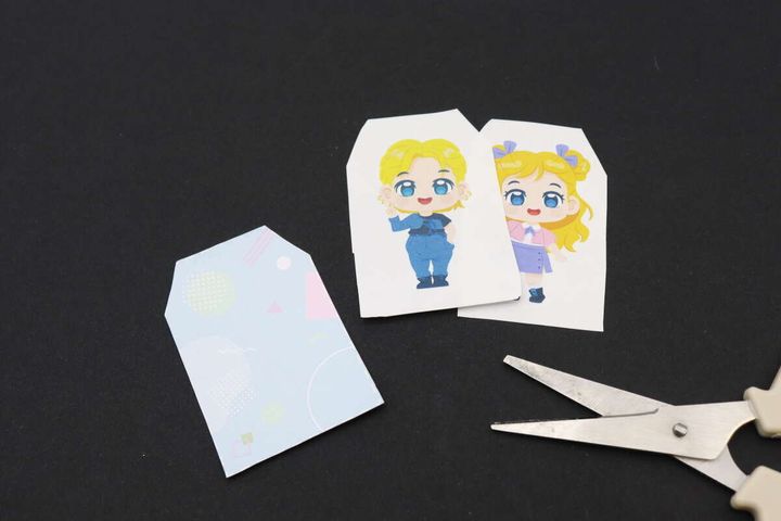 切り抜かれたイラストと、切り抜く前のパッケージ台紙、ハサミが黒い背景に置かれている