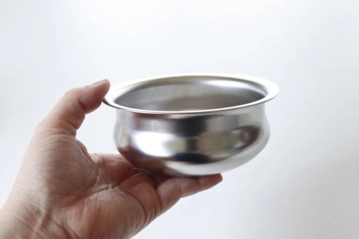 女性の手で持たれた丸みのあるステンレス製カレーポット