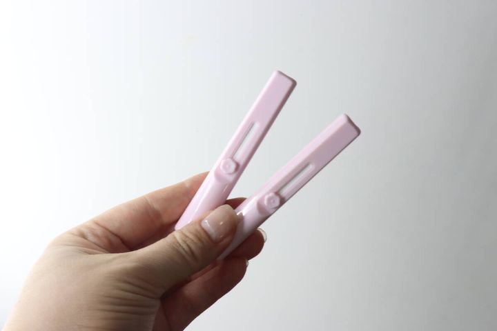 女性がピンク色のスライド式メイクブラシ2本を指で挟んで持っている
