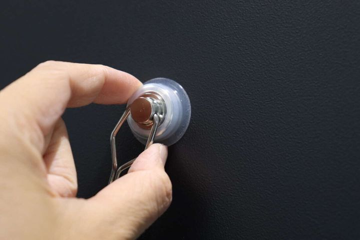 黒い壁に磁石フックを取り付け、指で固定している様子