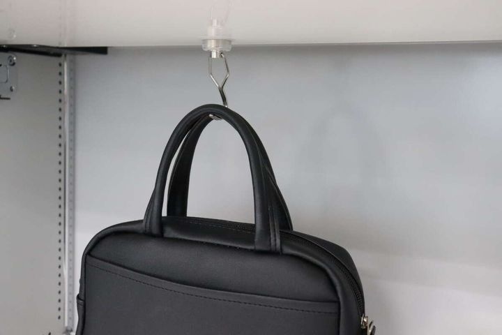 ロッカーの天井に吊るした磁石フックに黒いカバンを掛けている