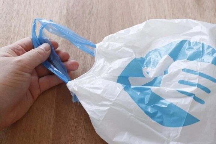 白いポリ袋の青いひもを引っ張って口を閉じている手元