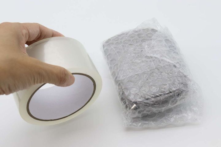 透明な梱包テープのロールと、緩衝材で包まれた小物が並んでいる