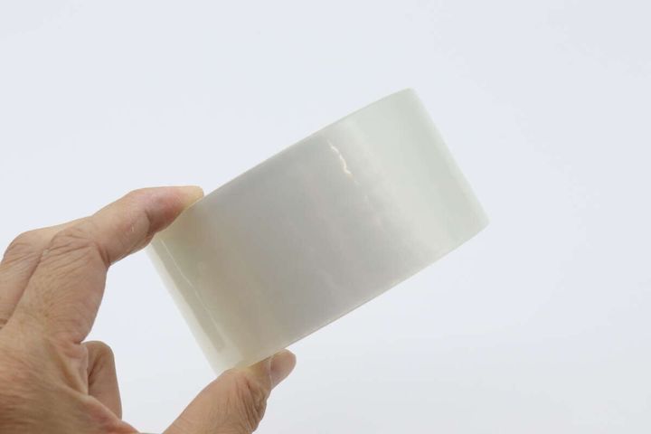 透明な梱包テープのロールを右手が横から持っている様子