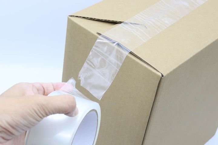 ダンボール箱に透明な梱包テープを貼り、手でちぎっている途中
