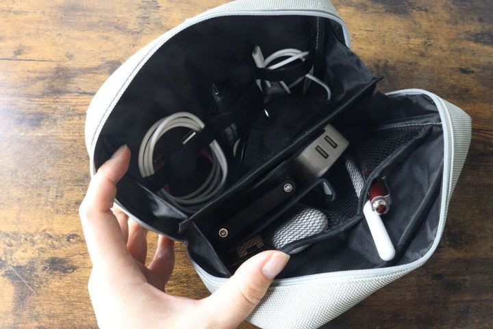 女性の手がガジェットポーチを開き、ケーブルやアダプター、ペンなどが収納されている