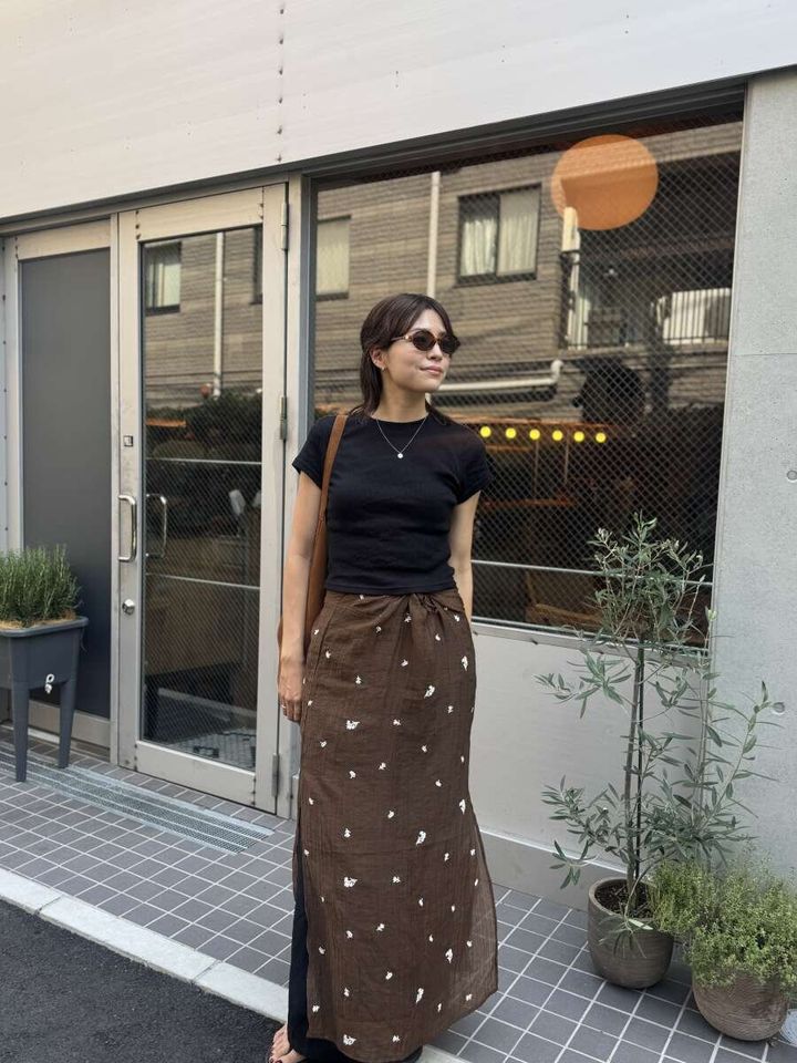 黒いミニTとブラウンのロングスカートを着用した女性が、店の前で立っている