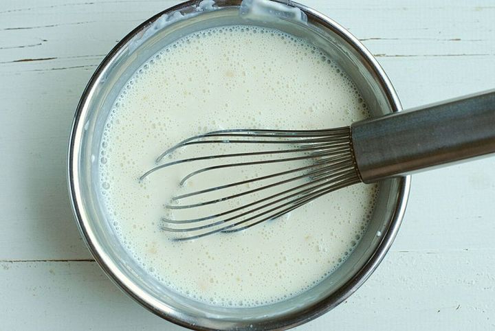ステンレス製のボウルに入った豆腐と豆乳の混合液を泡立て器で混ぜている様子