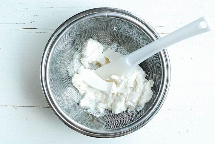 ボウルの上に置かれたザルで絹ごし豆腐をゴムベラで押し潰し、なめらかにしている様子