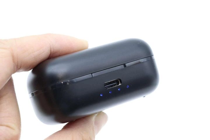 指で持った黒いワイヤレスイヤホンの充電ケース。充電ポートと青いLEDが見える
