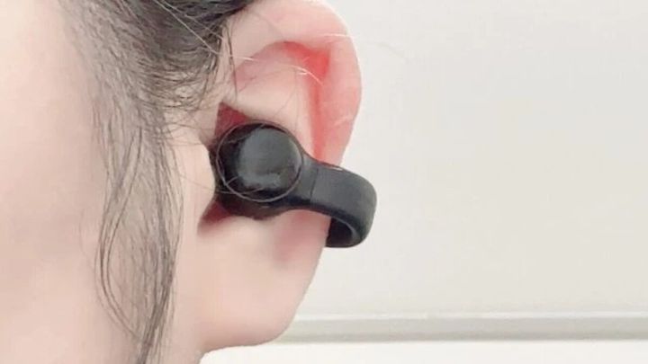 女性の耳に装着された、耳穴を挟むタイプの黒いワイヤレスイヤホン