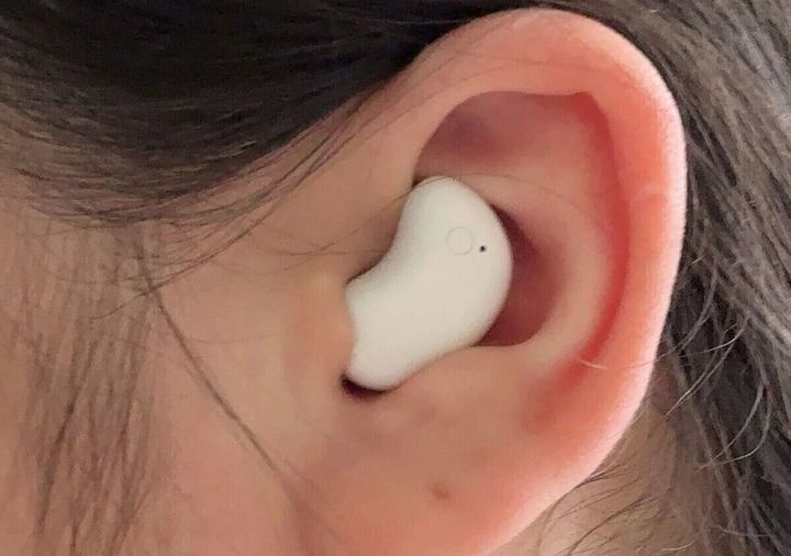 女性の耳に装着された、薄型で耳にフィットする白い寝ホン