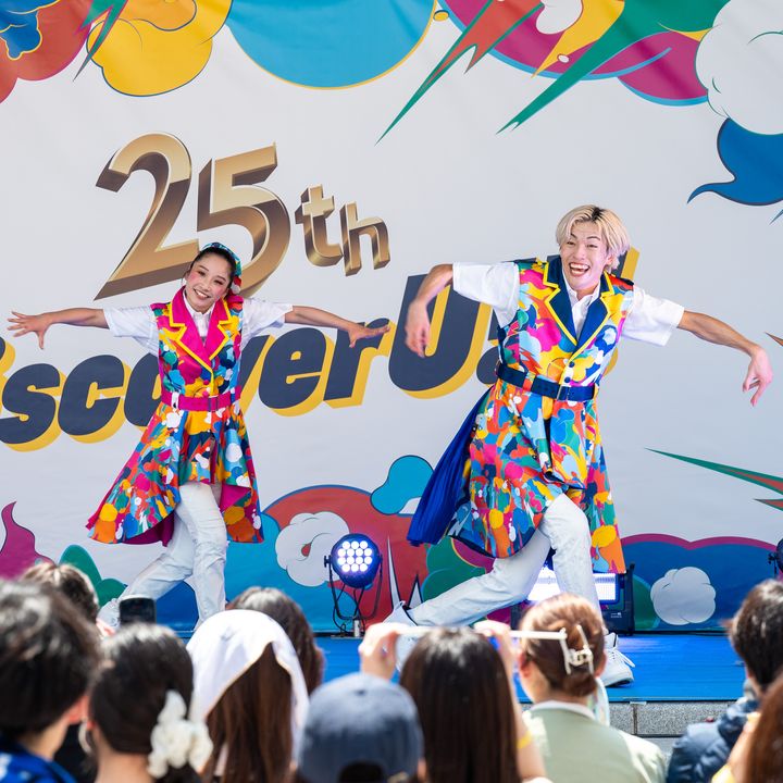 「25th Discover U!!!」のバナー前でポーズを取るエンターテイナー