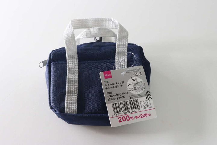 紺色のミニスクールバッグ風チャームポーチが白い背景に置かれ、商品タグが付いている