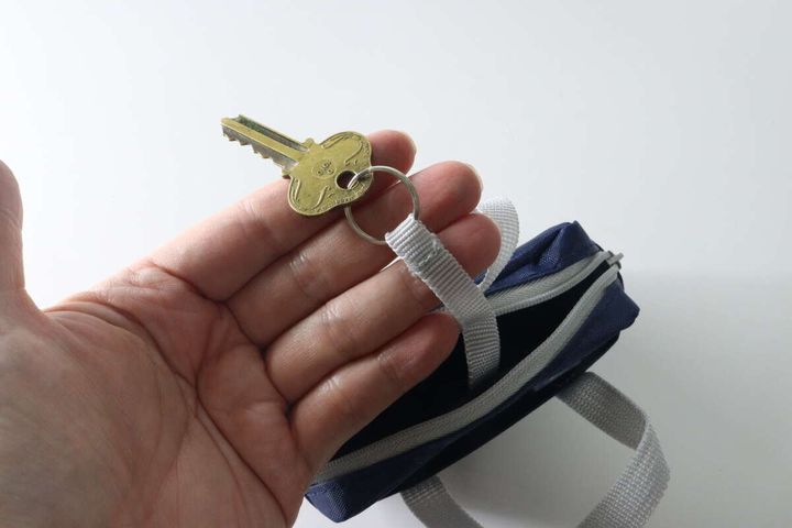 手がポーチのキーリングに鍵を取り付けている様子
