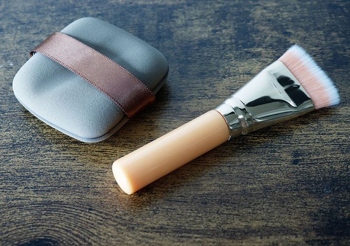 木目調のテーブルに置かれた、ケースから出した状態のメイクパフとメイクブラシ