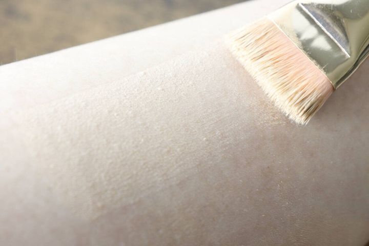 女性の腕に、メイクブラシを使ってパウダーファンデーションを薄く塗布している様子