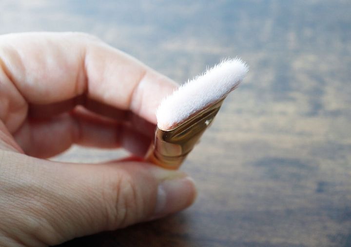 女性の手が、毛先が白く平らな形状のメイクブラシを横から持っている様子