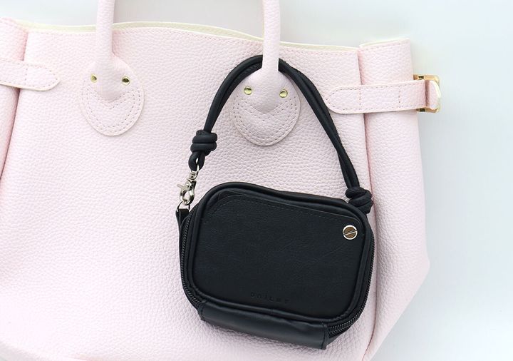 ピンク色のバッグの持ち手に黒いコンパクトポーチを付けている