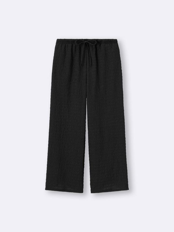 黒のシャーリングアンクルパンツ。フレアシルエットでスタイルアップ効果。