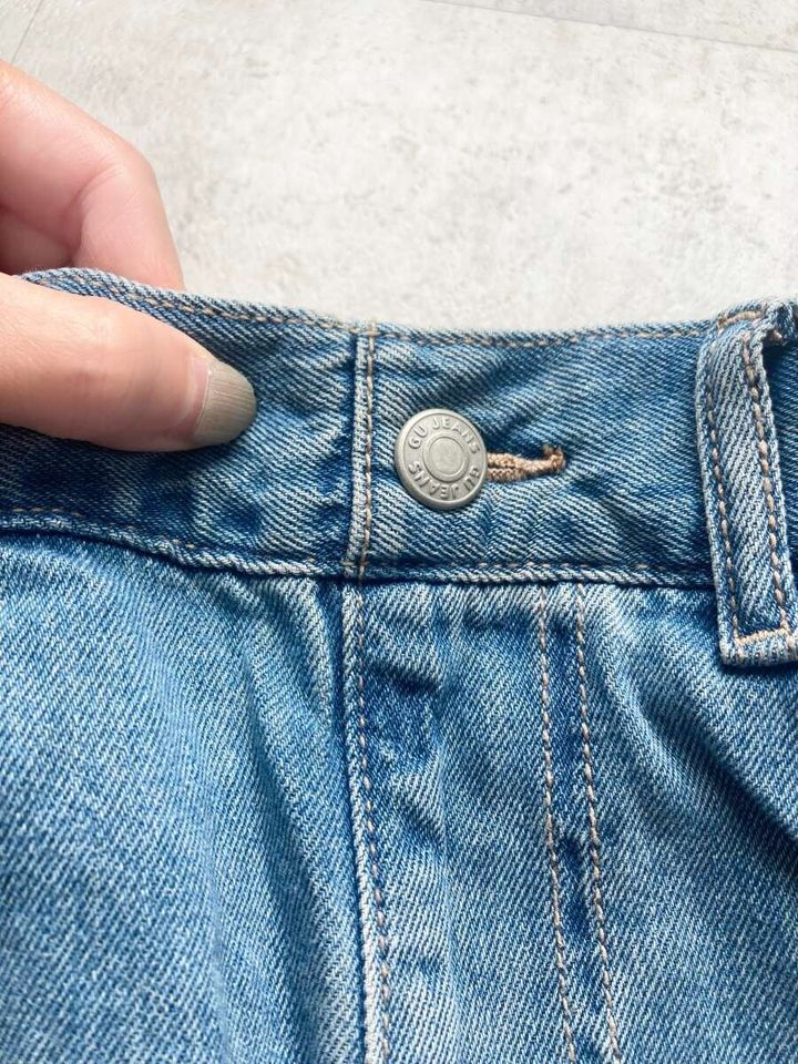 GU JEANSと刻印されたデニムのボタンを指でつまんでいる