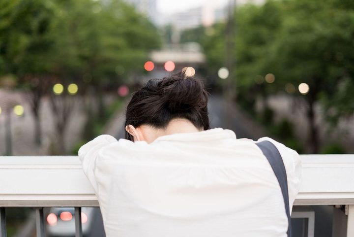 歩道橋の手すりに顔をうずめて落ち込んでいる女性