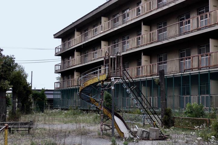 古い団地の敷地にある錆びたすべり台と、雑草が生い茂る広場。