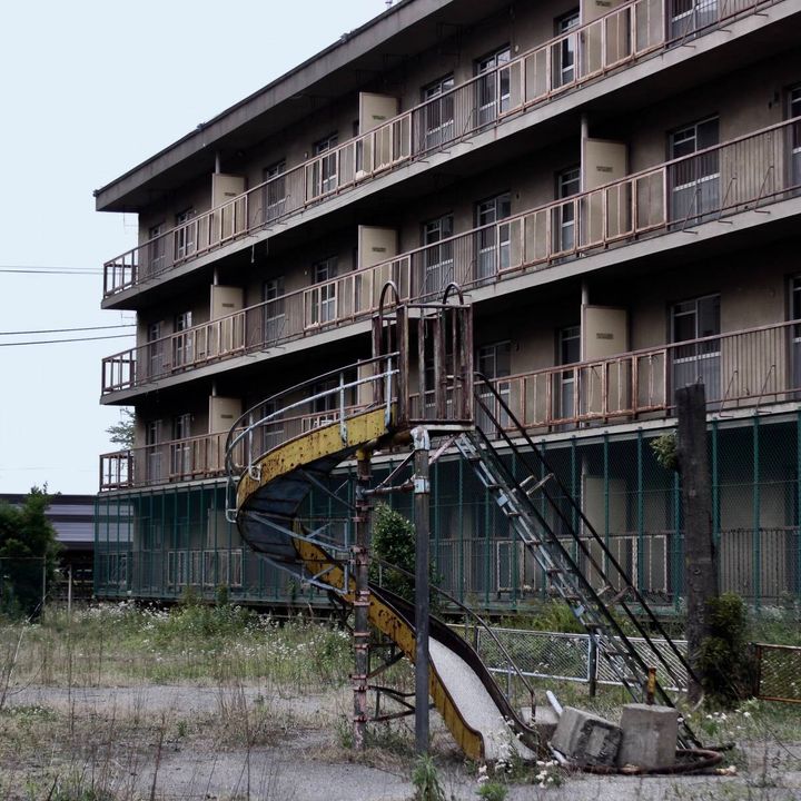 古い団地の敷地にある錆びたすべり台と、雑草が生い茂る広場。