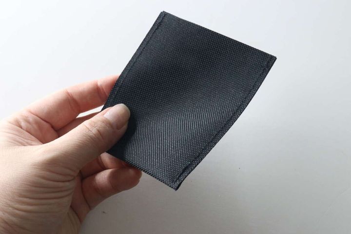 女性の指が黒い布製のポケット本体をつまんでいる