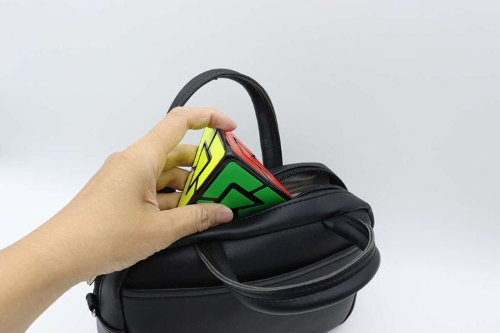 女性の手がピラミッド型パズルを黒いバッグに入れている