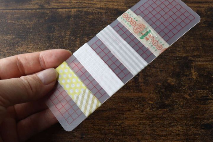 数種類のマスキングテープが巻きつけられた巻き板を手に持っている