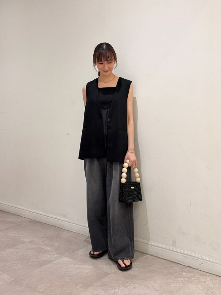 黒いジレと黒いワイドデニムを着用し、ビーズバッグを持った女性